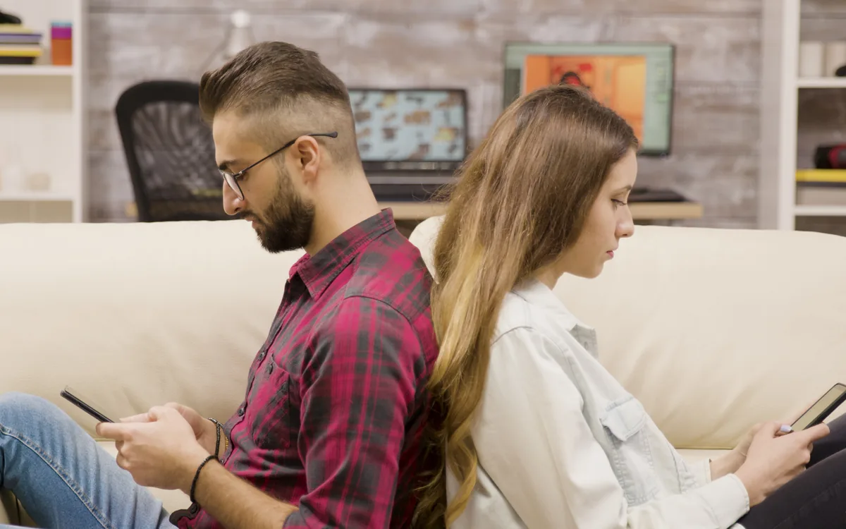 Pareja sentada de espaldas en el sofá, cada uno con su teléfono: problemas de pareja y alejamiento que Don Jacinto trabaja con limpias y rezos